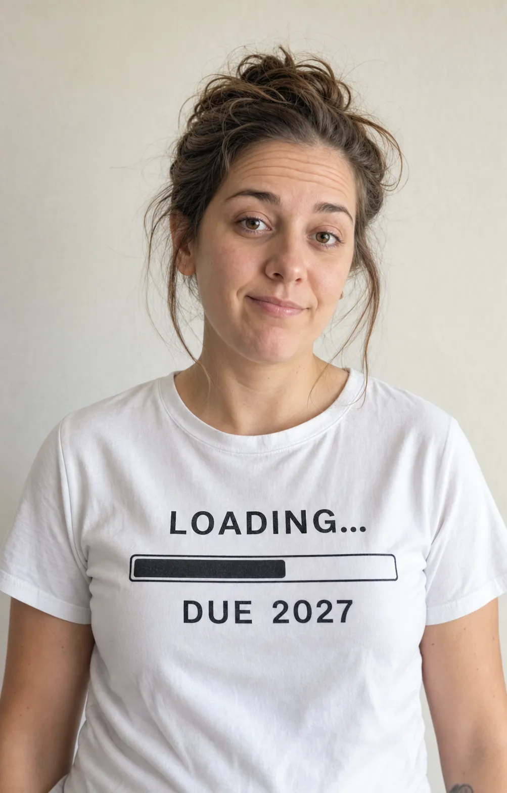 Same uploaded photo, vibe three: a deadpan portrait against a plain wall in a white tee printed Loading, Due 2027 with a half-filled progress bar.