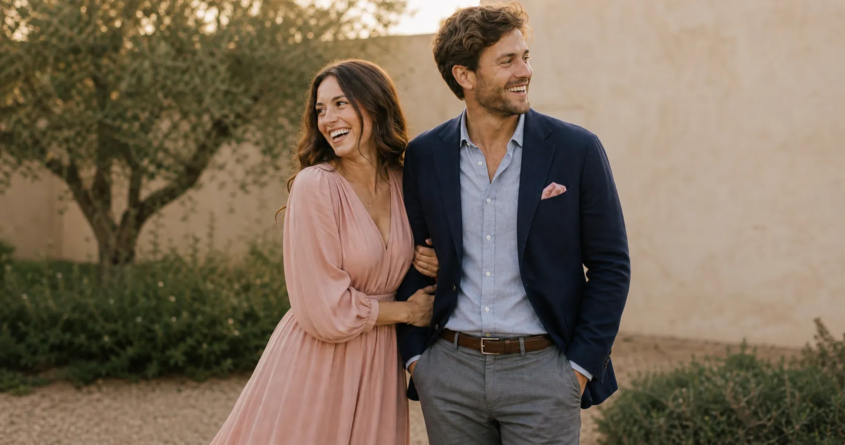 An engaged couple showing the statement and anchor method: she leads in a blush dress, he anchors in navy and gray with a small blush accent, one shared palette worn two ways.