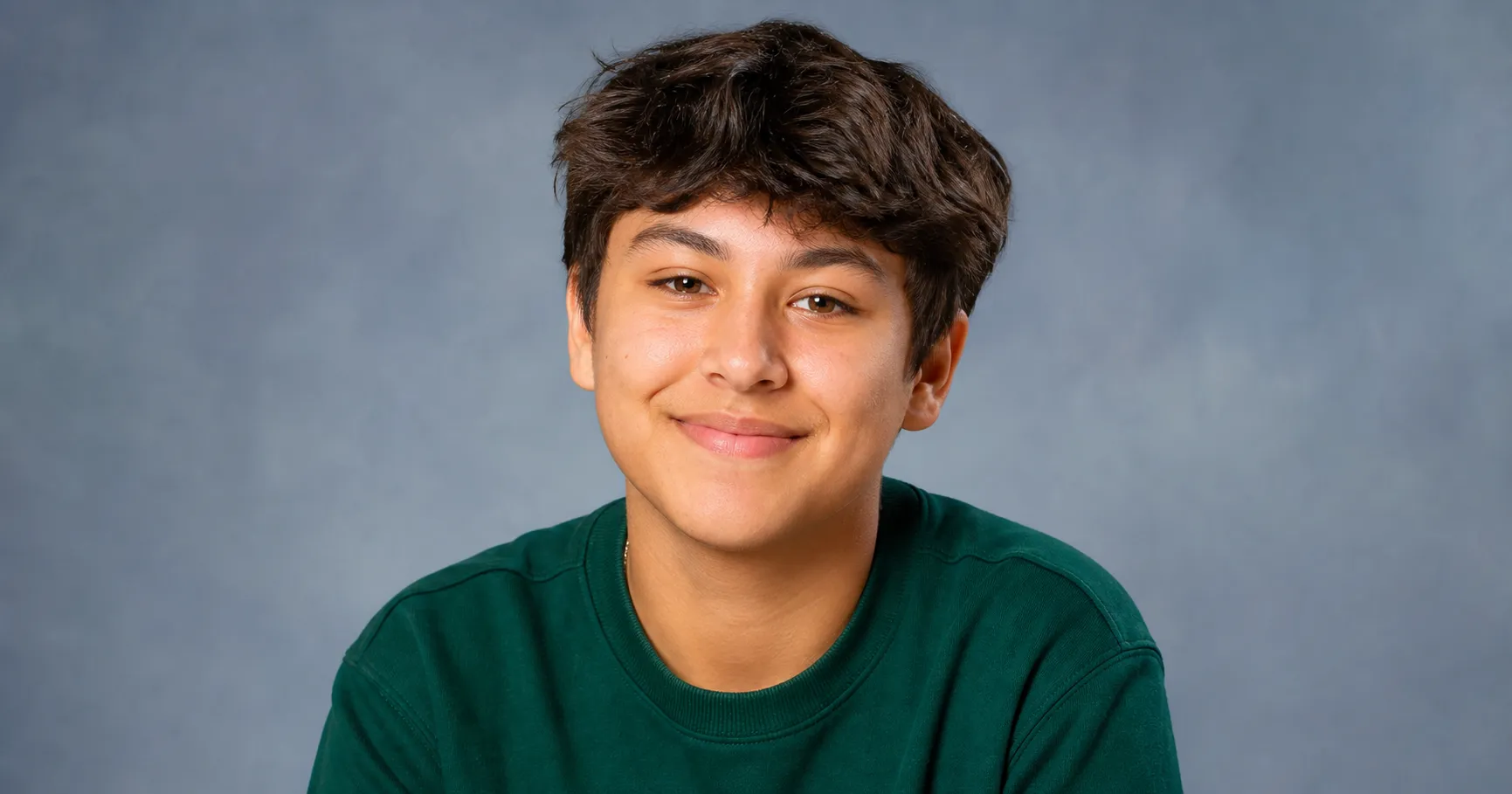 A student in a solid jewel-tone top sitting for a picture-day photo in soft front light, chin slightly forward and a relaxed genuine smile.