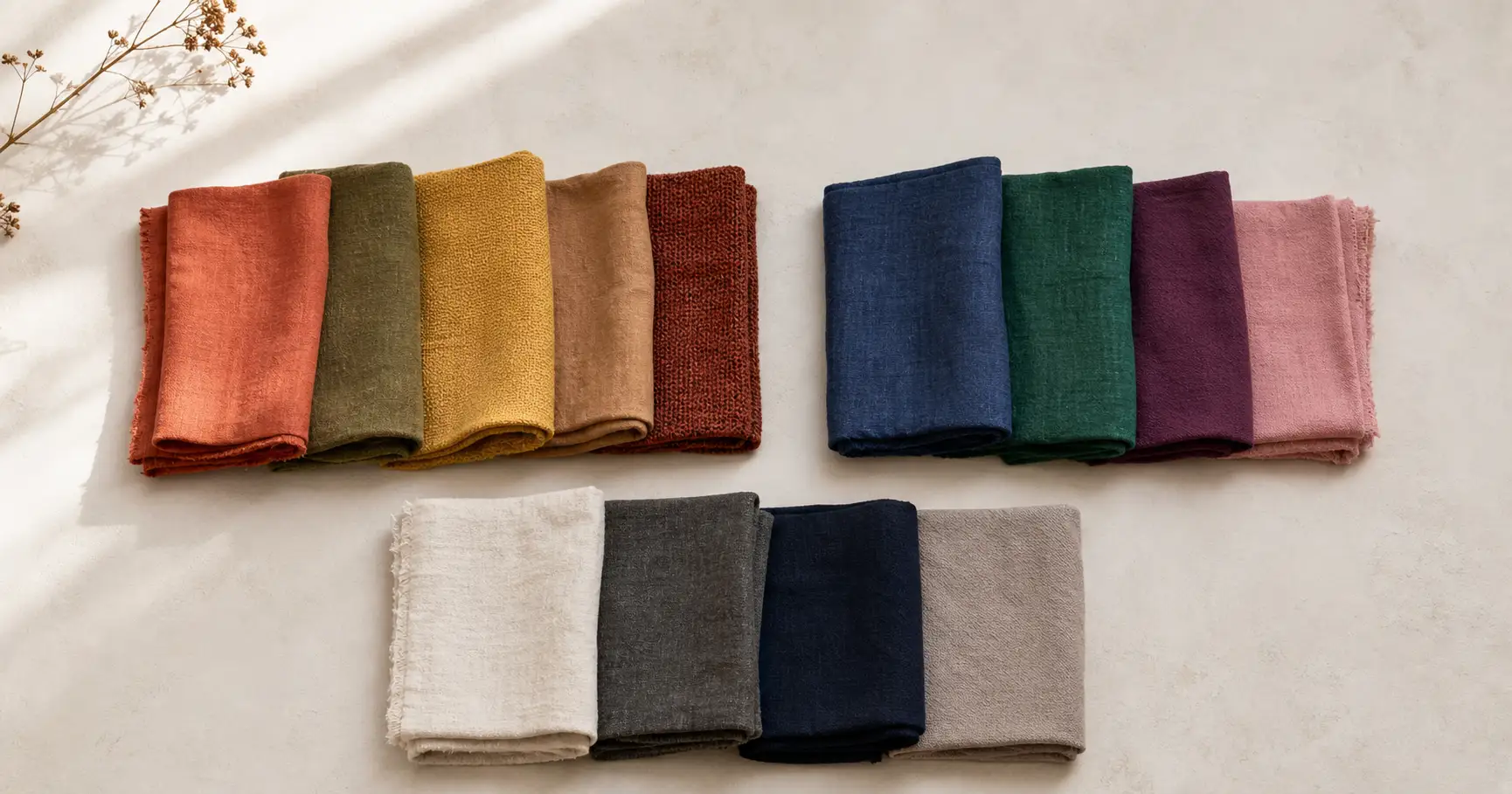 A flat-lay of fabric swatches sorted into three color families, warm earth tones in terracotta olive and mustard, cool jewel tones in sapphire emerald and plum, and a row of neutrals in cream charcoal and navy, arranged in soft daylight.