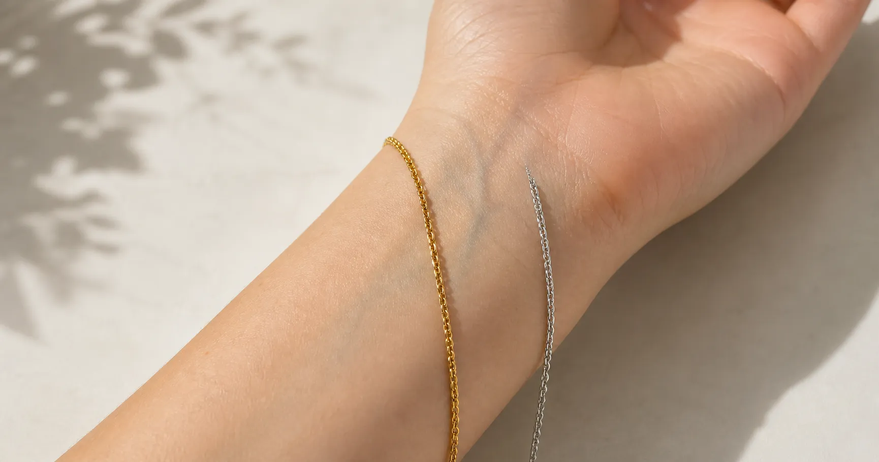 A gold bracelet and a silver bracelet held against the inside of a wrist in daylight, the gold warming the skin and the silver cooling it, showing the gold-versus-silver undertone test.