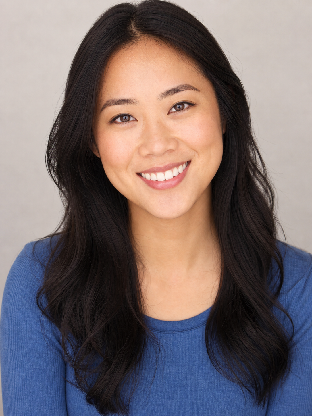 A commercial acting headshot example: bright even lighting, a warm natural smile, a clean light backdrop, and a simple solid top, reading as approachable and trust-me.