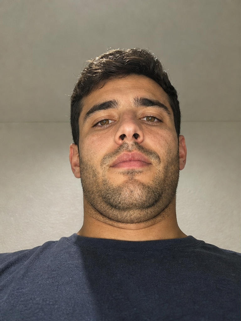 A man's selfie with the phone held low under flat overhead light, distorting his face and stacking his chin.