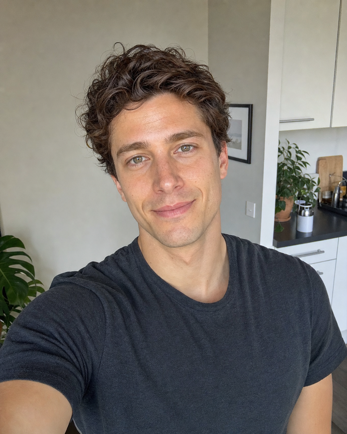 Dating profile photo example #1: a soft-natural-light close-up candid selfie of a 30-year-old person taken on an iPhone at home with a half-smile and direct eye contact, deliberately styled to read as a real photo rather than an AI render, identity-locked 4:5 dating-app primary photo format.