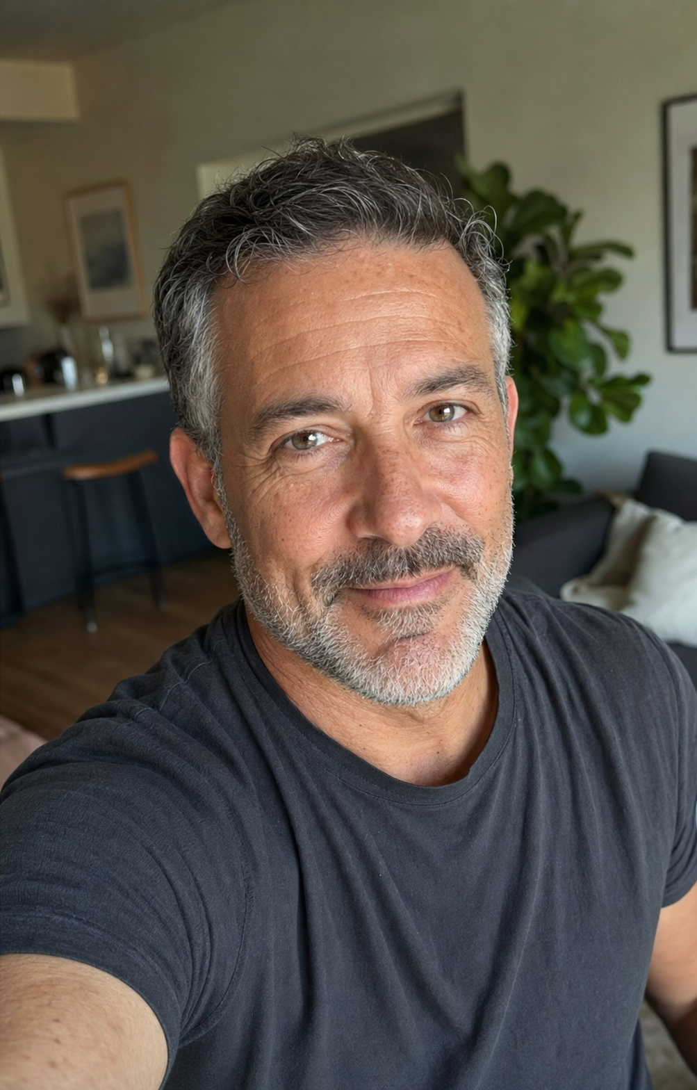 A 52-year-old man rendered with the aging-preservation rule line applied, showing genuinely half-grey salt-and-pepper hair, visible nasolabial lines, soft under-eye area, light expression lines around the eyes, and natural mid-50s skin texture — the actual face that walks into a cafe on date day, the rule-following state the article argues for.
