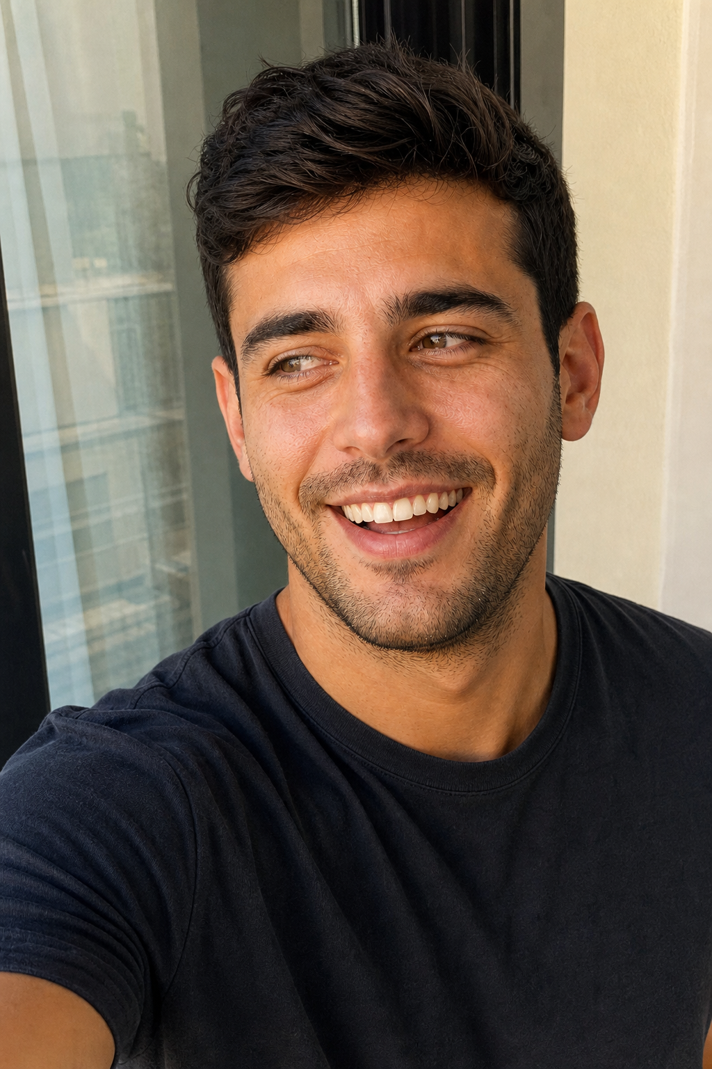 A man's candid-feeling selfie, caught mid-laugh looking just off the lens in warm natural light.