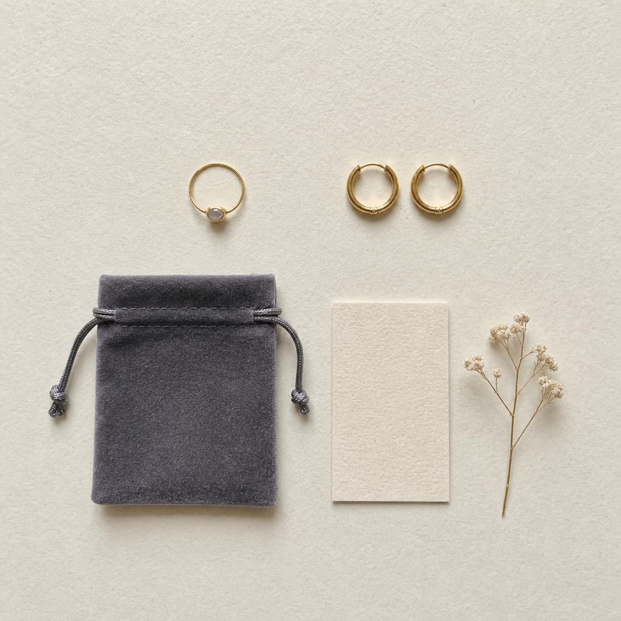 Top-down knolling flat-lay of a handmade Etsy jewelry order on textured cream paper — a delicate gold ring, gold hoop earrings, a charcoal velvet pouch, a cream care card, and a small dried botanical sprig — AI-generated example of the slot-4 what's-included listing photo for a jewelry maker.